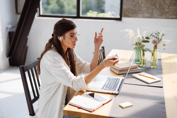 istock Freelancer in earphone having video call on laptop while working near notebooks at home 2158070912