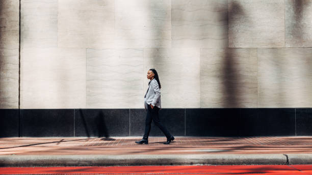 Businesswoman Walking Along Urban Street in Daylight Confident businesswoman walking along a sunlit urban street, exuding professionalism and purpose under the clear sky. african american architecture stock pictures, royalty-free photos & images