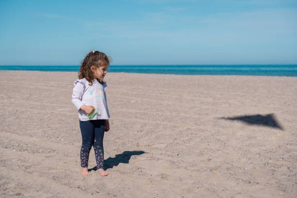 little girl flying a kite on the beach, looking at the kite's shadow on the sand