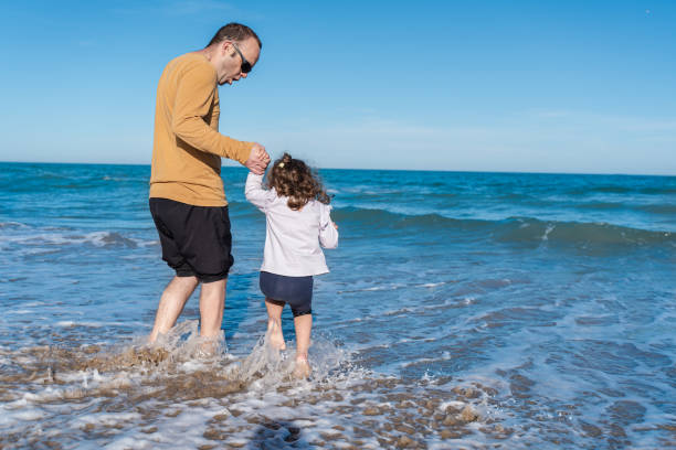 father and daughter enjoying a sunny day at the beach jumping waves on the shore