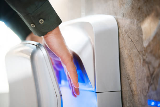 Hand taking paper towel from a dispenser in a clean public restroom with white tiles.