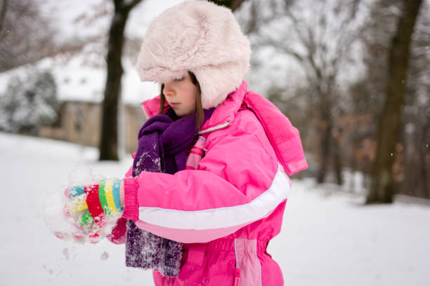 Side view of a cute girl in warm clothing playing whit snow in park