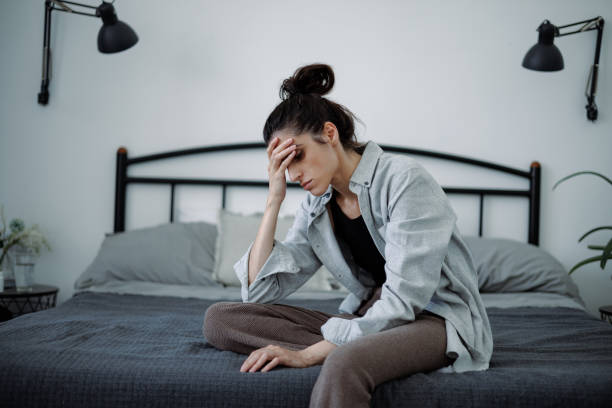 istock Disappointed brunette woman touching forehead while sitting on bed at home 2158076976