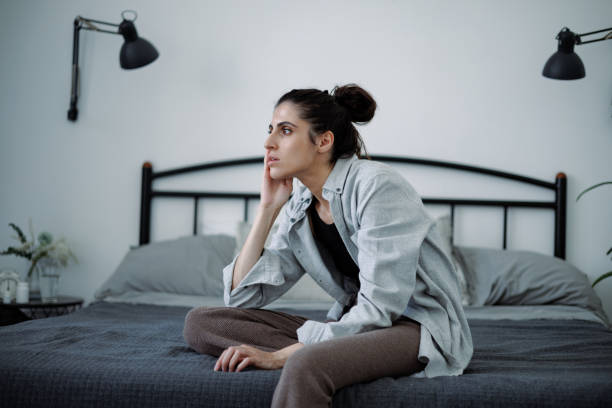 istock Woman with depression looking away while sitting on bed at home 2158076985