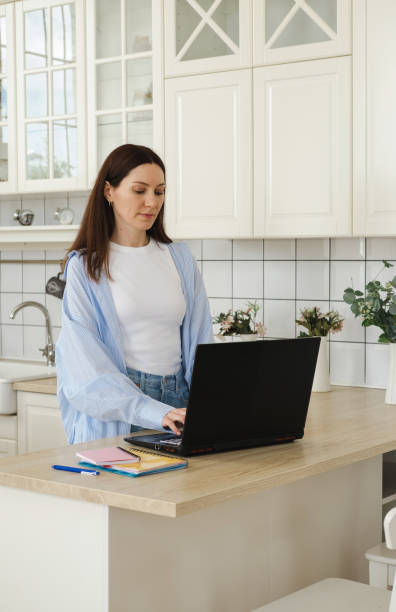 istock Portrait of a woman using laptop while working remotely from home in kitchen. Remote work, freelancer workplace at kitchen table. Motherhood and career, freelancing and homeschooling 2158077811