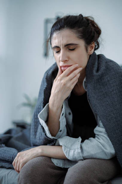 istock Depressed brunette woman wrapped in blanket touching chin while feeling sorrow while sitting on bed 2158078629