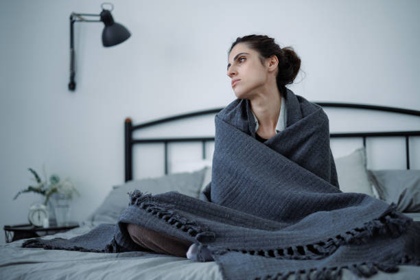 istock Frustrated brunette woman wrapping in blanket while sitting on bed at home 2158078739