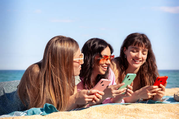istock Three happy young friends on the beach using apps on their smartphones 2158078767