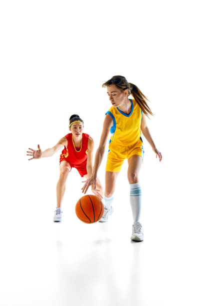 istock Competition and agility. Dynamic image with young women in red and yellow uniform in motion, playing basketball isolated on white studio background 2158080115