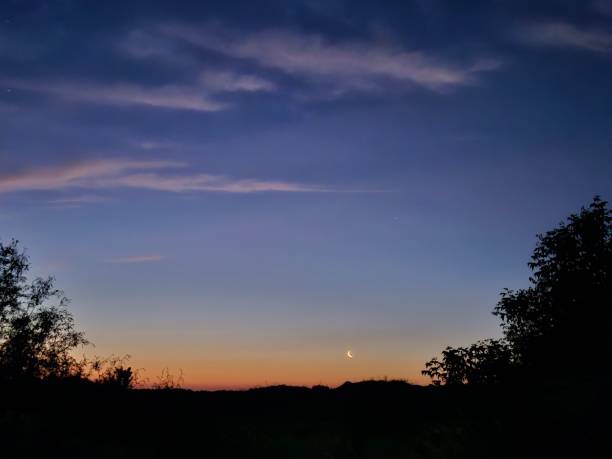 istock Serene sunset landscape with a crescent moon and silhouetted trees 2158084449