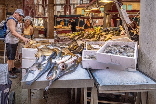 Venice, Italy - June 5th 2024:  Customers looking at the fresh fish at a market stall in the open air food market in the center of Venezia