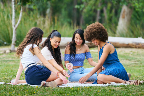 istock Four women are sitting on a blanket in a park, playing a game 2158091074