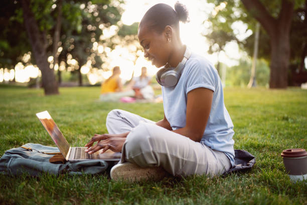 istock Side-view of a young woman Black ethnicity, using the laptop for work or studying, while sitting on grass 2158092448