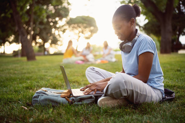 istock Side-view of a young woman Black ethnicity, using the laptop for work or studying, while sitting on grass 2158092467