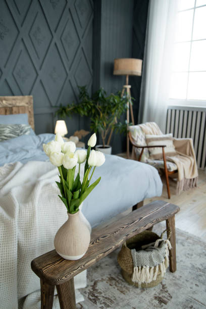 istock Wooden bench with a vase of white tulips as the main focus. Surrounding elements include a cozy bed with blue linens, sheer curtains, and a wicker basket on a patterned rug 2158093073