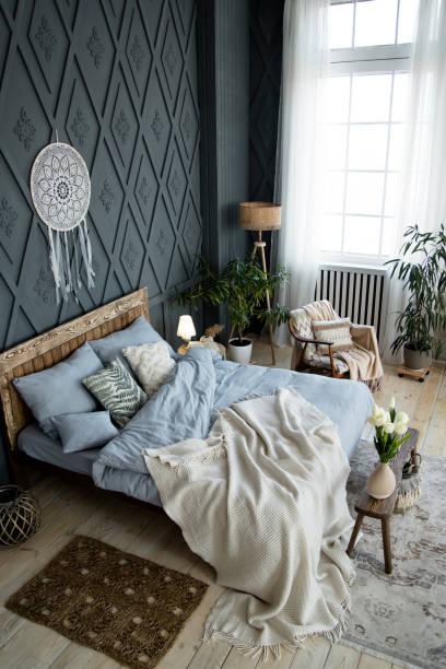 istock Stylish bedroom setup includes rustic wooden bed, soft blue bedding, and decorative pillows. Wicker accents, indoor plants, and a large window enhance the serene environment. Dreamcatcher on wall 2158093836