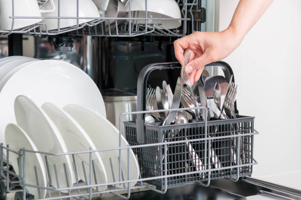 istock Female hand unloading dishwasher with tableware. Kitchen appliances, lifestyle view. Woman takes a fork from the dishwasher. Concept of modern technologies in the kitchen 2158100258