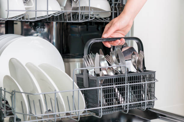 istock Female hand unloading dishwasher with tableware. Kitchen appliances, lifestyle view. Woman takes a cutlery basket from the dishwasher. Concept of modern technologies in the kitchen 2158100274