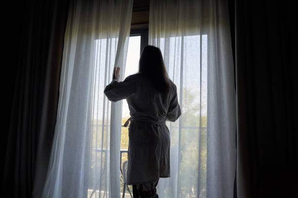 istock Woman in Bathrobe Opening Curtains to Morning Light 2158101838