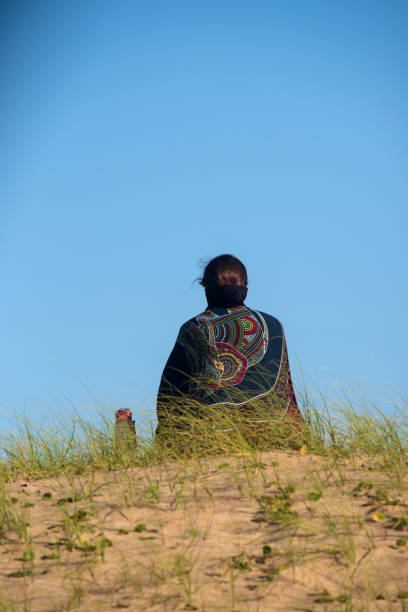 Woman seen from behind sitting on top of a dune observing the landscape