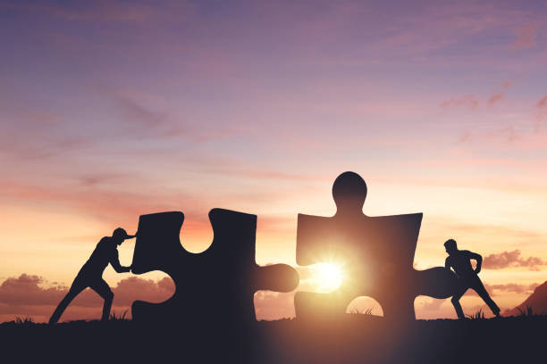 istock Silhouette of a team folding a puzzle against a sunset background, business and teamwork concept 2158102027