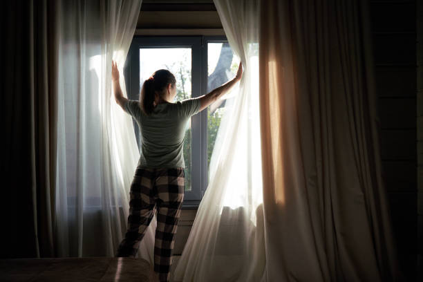 istock Woman Drawing Curtains Open in Morning Light 2158102060