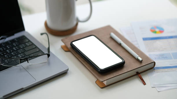 istock Smartphone with blank screen, laptop and financial document on white office desk. 2158106253