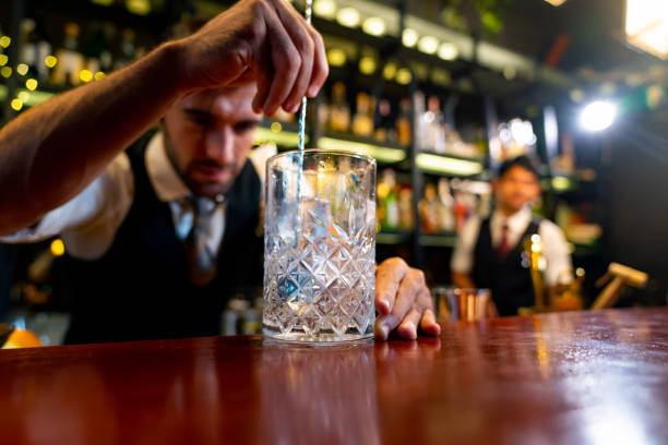 Male bartender preparing alcoholic drink at restaurant bar. Professional man bartender preparing cocktail drink in cocktail glass serving to customer on counter at luxury restaurant bar. Barman making mixed alcohol drink celebration holiday party at nightclub. restaurant labor union stock pictures, royalty-free photos & images