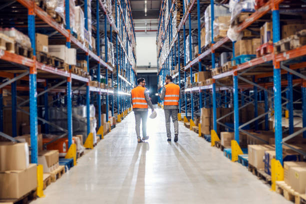 istock Two businessmen walking trough storage full of goods and boxes. Commodity reserves concept. 2158111805