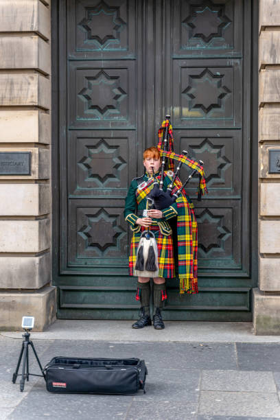 Male bagpipe player in kilt and ceremonial dress busking in Edinburgh city doorway on Lawnmarket street near the entrance to Edinburgh Castle.