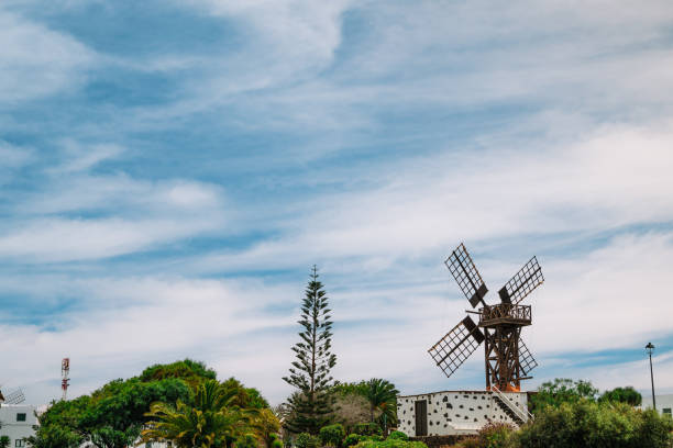 A windmill is standing in a field with a cloudy sky in the background. The windmill is old and rusted, giving the scene a nostalgic and somewhat melancholic mood
