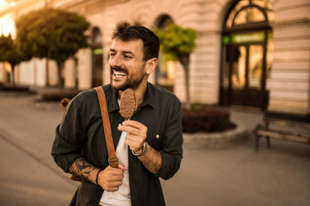 Cheerful young man enjoying Ice Cream while on a walk in the city on summer day.
