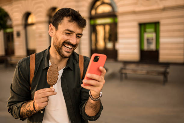 istock Happy young man using phone and eating Ice Cream while exploring the city. 2158125038