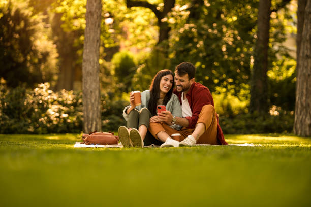 istock Happy young couple using phone while relaxing together at a park on summer day. 2158125664