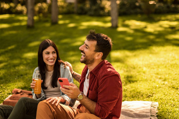 istock Happy young couple using phone while having fun and laughing at a park on summer day. 2158125717