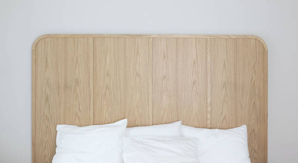 Modern luxurious bedroom with large empty double bed. White linens, pillows. Comfortable sleep. Oak wooden headboard. Grey wall background. Trendy elegant interior. Hotel, accomodation concept.
