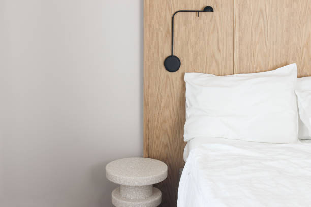 istock Scandinavian style bedroom with large empty double bed. White linens, pillows. Modern night table, black wall lamp. Comfortable sleep. Oak wooden headboard. Grey wall background. Hotel, accomodation 2158138628