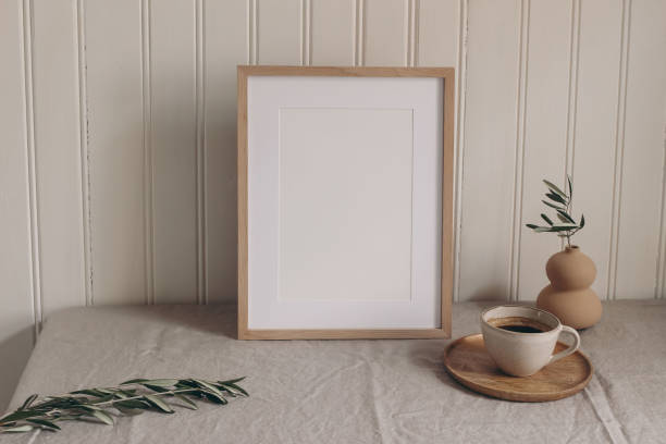istock Vertical wooden picture frame mockup on linen table cloth. Vase with olive branches, cup of coffee on table. White wooden beadboard wall panelling background. Elegant home interior decor still life. 2158138638