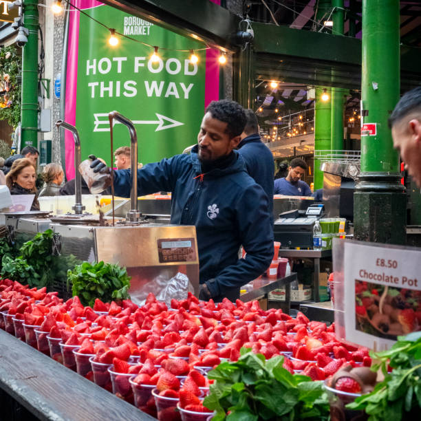 A stall-holder preparing to coat strawberries in chocolate in Borough Market, Southwark, London.