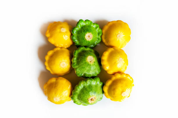 A vibrant assortment of yellow and green pattypan squashes arranged on a white background. This colorful and fresh produce is perfect for healthy cooking, adding a touch of summer harvest to any meal.