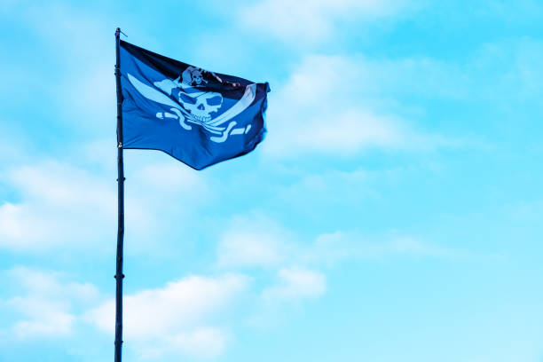 A black pirate flag with a skull flutters against a blue sky background. High quality photo