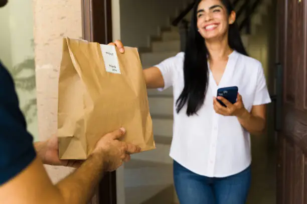 Closeup of a joyful latin woman accepting a food delivery in a brown paper bag at her doorstep Closeup of a joyful latin woman accepting a food delivery in a brown paper bag at her doorstep