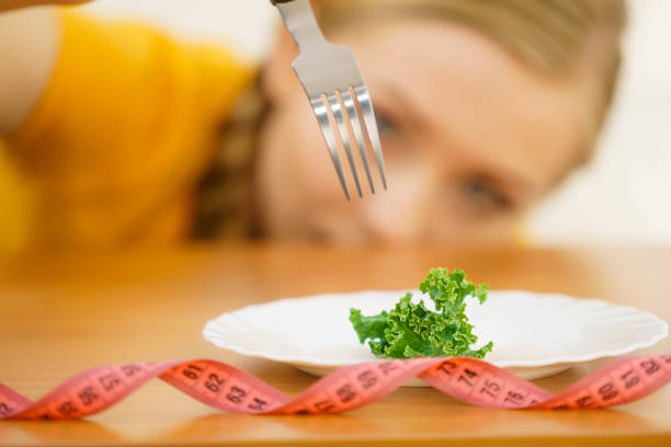 Sad young blonde woman dealing with anorexia nervosa or builimia having small green vegetable on plate. Dieting problems, eating disorder.