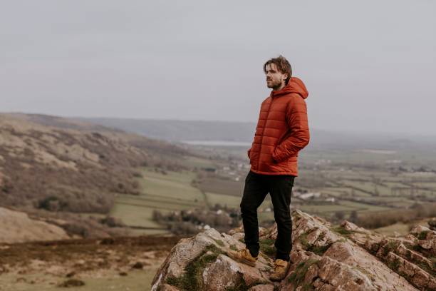 istock Man in orange puffer jacket, standing on mountain 2158176715