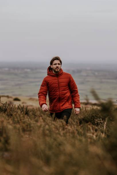 istock Man wearing orange puffer jacket, walking on hill 2158176886