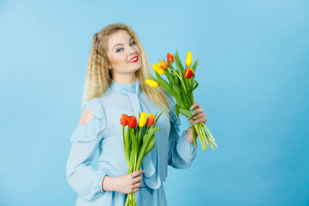 International women day, eight march. Beautiful portrait of pretty woman blonde hair with red yellow tulips, fashion make up, elegant dress. Mother day. On blue