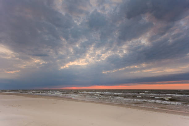 Beautiful idyllic landscape of sea and sandy beach during cloudy autumnal sunset.