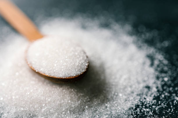 Wooden spoon of sugar top view on black background, splash.