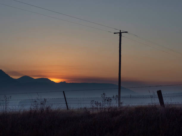 Powerline and farm fence in silhouette at sunrise