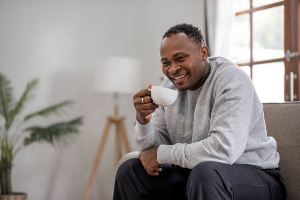istock African American man smiling while drinking coffee on sofa at home, Concept of relaxation 2158189380